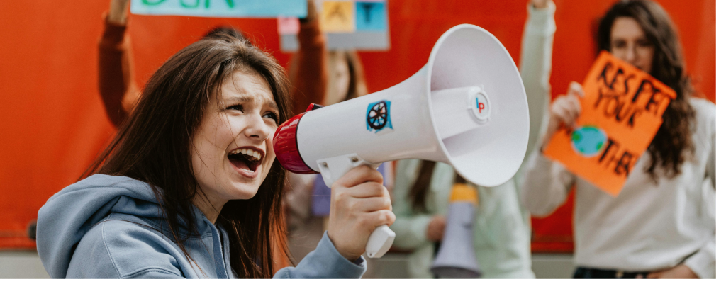 Eine Junge Frau spricht auf einer Demonstration in ein Megafon.